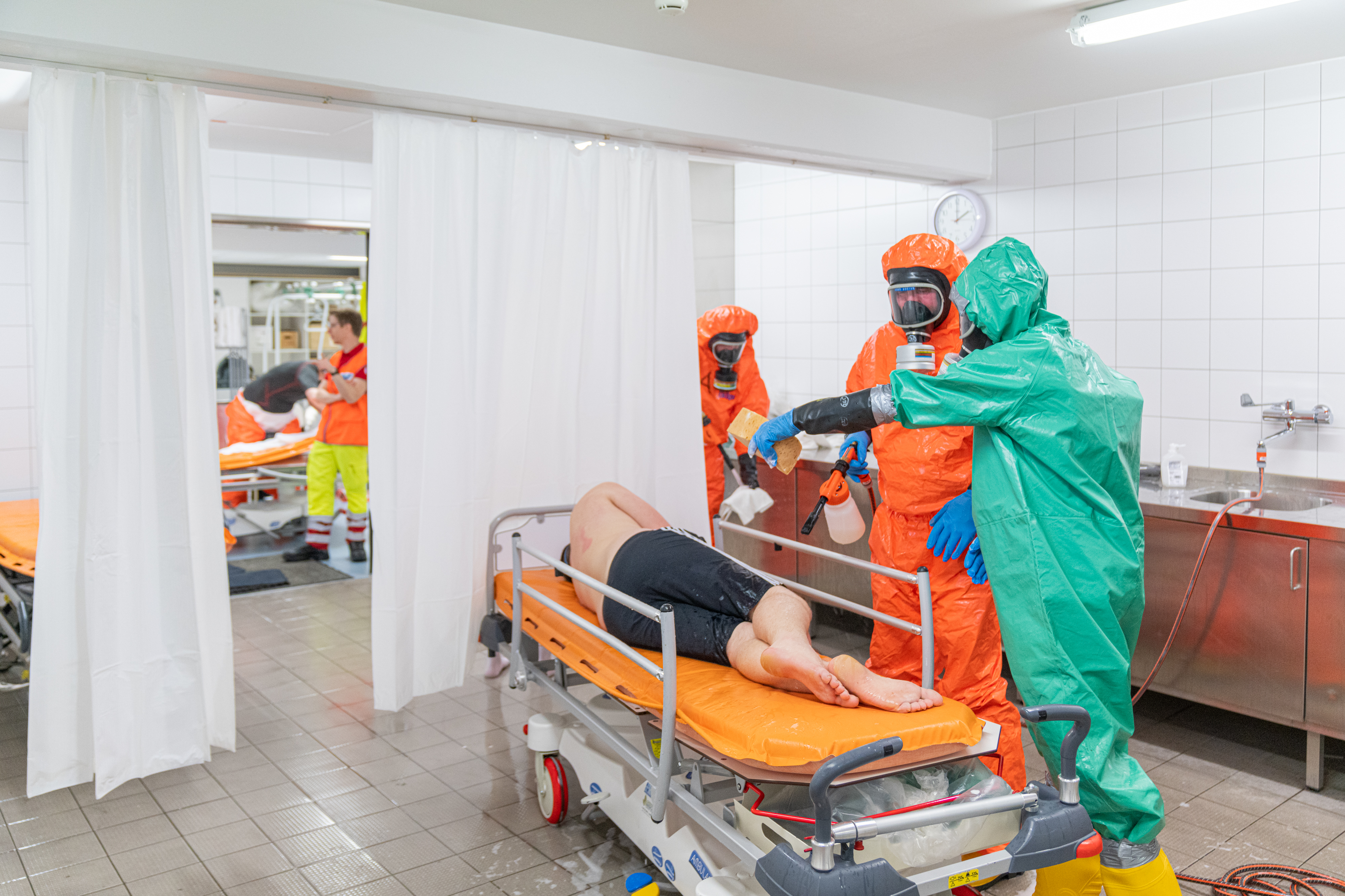 Ein Patient liegt im Zuge des Katastrophenschutzes in einem Zelt, Mitarbeiter:innen in Schutzanzügen umsorgen ihn.